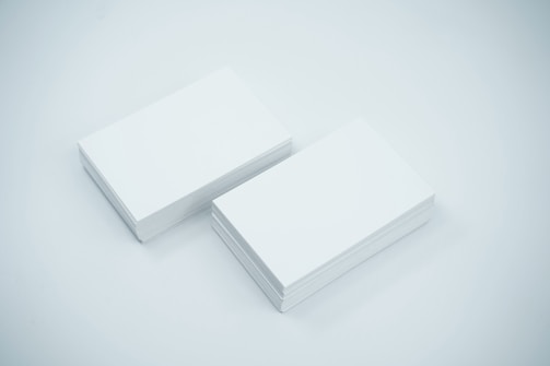 Two neat stacks of blank white business cards are placed side by side on a smooth, light-colored surface. The cards are uniformly aligned and appear crisp and clean.