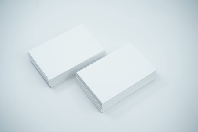 Two neat stacks of blank white business cards are placed side by side on a smooth, light-colored surface. The cards are uniformly aligned and appear crisp and clean.