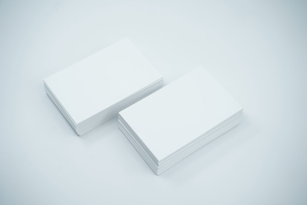 Two neat stacks of blank white business cards are placed side by side on a smooth, light-colored surface. The cards are uniformly aligned and appear crisp and clean.