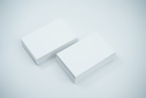 Two neat stacks of blank white business cards are placed side by side on a smooth, light-colored surface. The cards are uniformly aligned and appear crisp and clean.