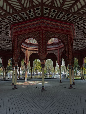 Handcrafted wooden gazebo with intricate carvings surrounded by blooming flowers.