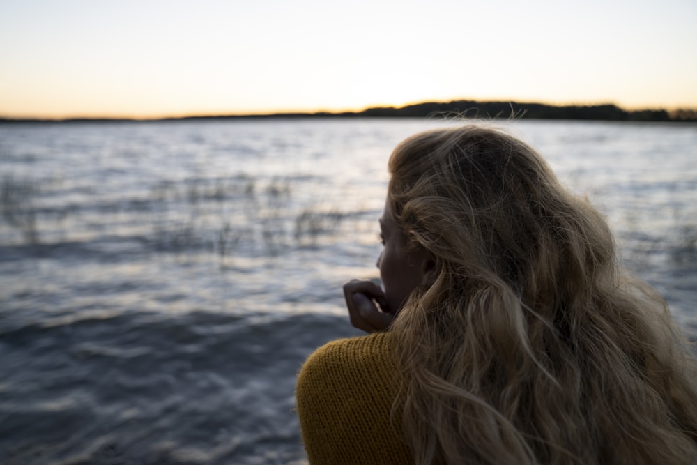 a woman with long blonde hair looking out at the water
