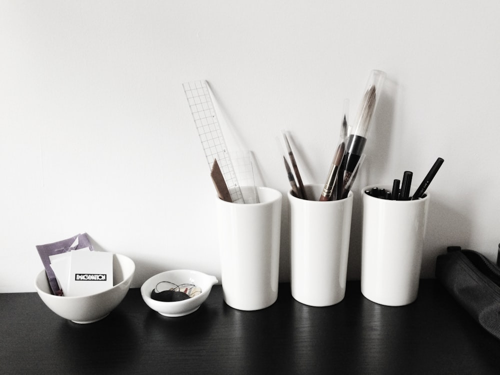 a black table topped with white cups filled with pens and pencils