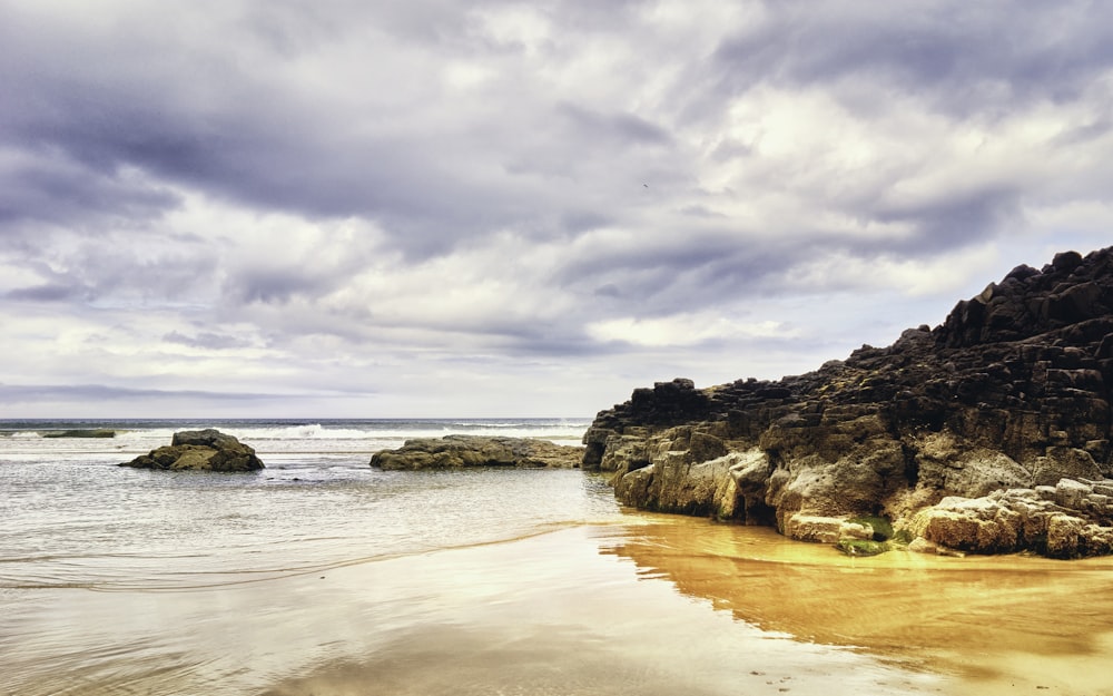 a sandy beach with rocks and water under a cloudy sky