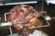 Close-up of a spit-roast with golden, crispy meat being carved by a chef in a bustling kitchen.