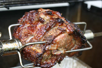 Close-up of a spit-roast with golden, crispy meat being carved by a chef in a bustling kitchen.