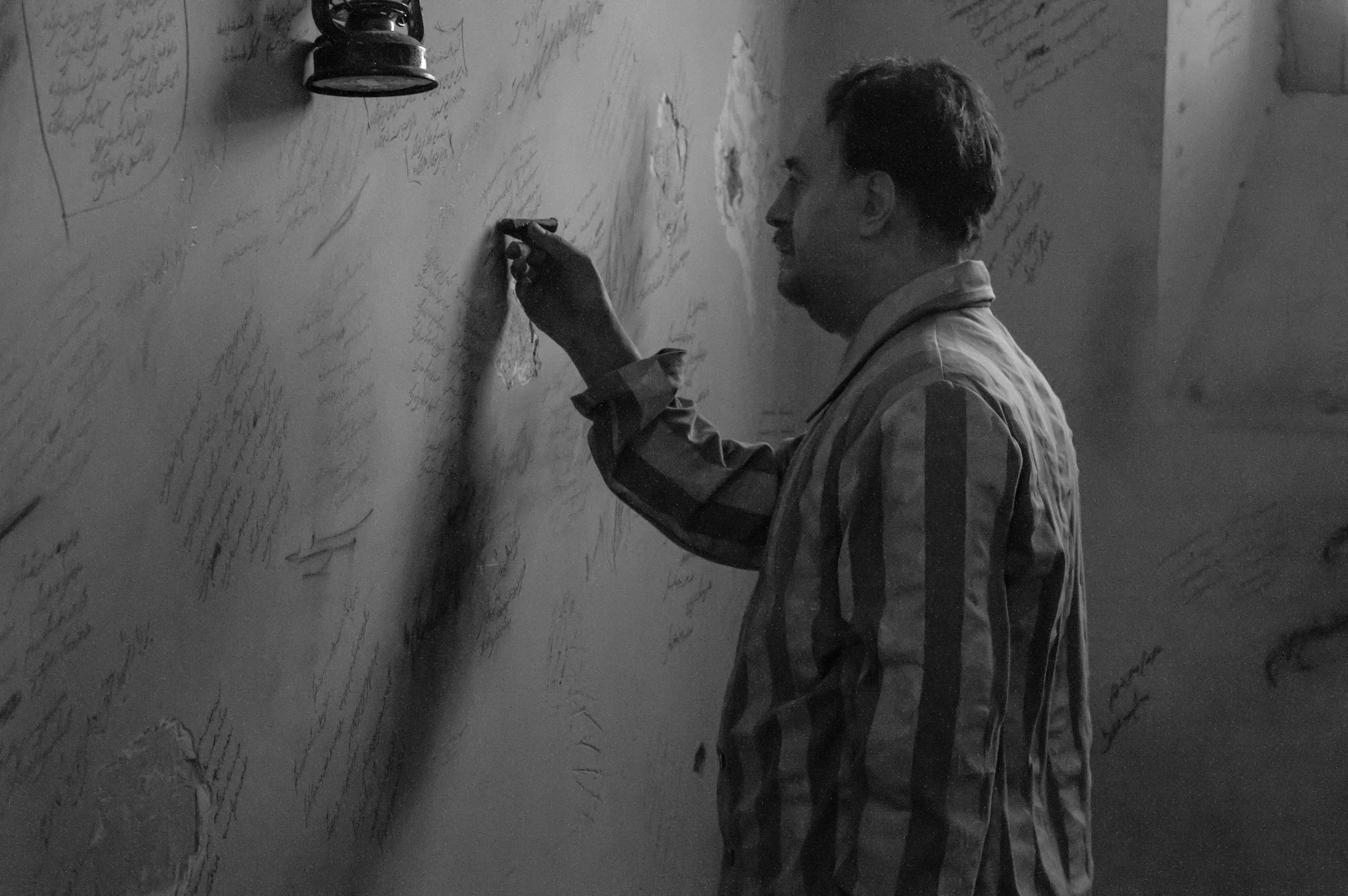 A man in a striped prison uniform writing on a wall already covered with the words of those who came before him