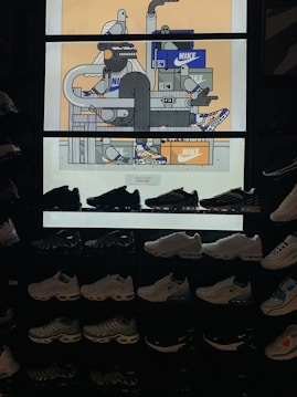 The image features a display of various Nike sneakers arranged on shelves. Above the sneakers is a vibrant, illustrated backdrop with expressive characters and Nike shoe boxes. The illustration depicts abstract figures and objects, incorporating geometric shapes and lines with a few cartoonish bird characters.