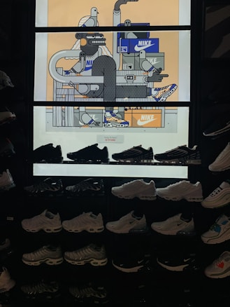 The image features a display of various Nike sneakers arranged on shelves. Above the sneakers is a vibrant, illustrated backdrop with expressive characters and Nike shoe boxes. The illustration depicts abstract figures and objects, incorporating geometric shapes and lines with a few cartoonish bird characters.