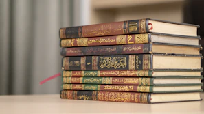 A stack of academic Islamic books with elegant green and gold covers on a wooden table.