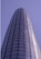 A tall, cylindrical skyscraper with a sleek glass facade extends upwards into a clear blue sky. Two window cleaners in red uniforms are visible on the exterior, highlighting the building's impressive height and modern architecture.