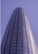 A tall, cylindrical skyscraper with a sleek glass facade extends upwards into a clear blue sky. Two window cleaners in red uniforms are visible on the exterior, highlighting the building's impressive height and modern architecture.