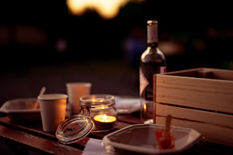 A rustic wooden table set outdoors with freeze-dried meals, camping gear, and a chef’s knife catching the golden hour light.