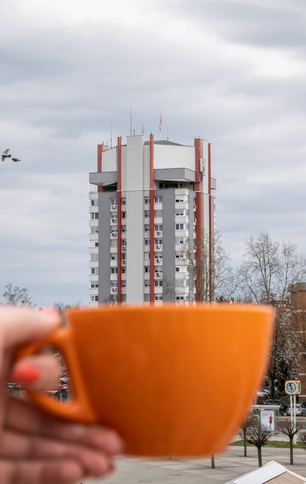 a person holding an orange cup in front of a tall building