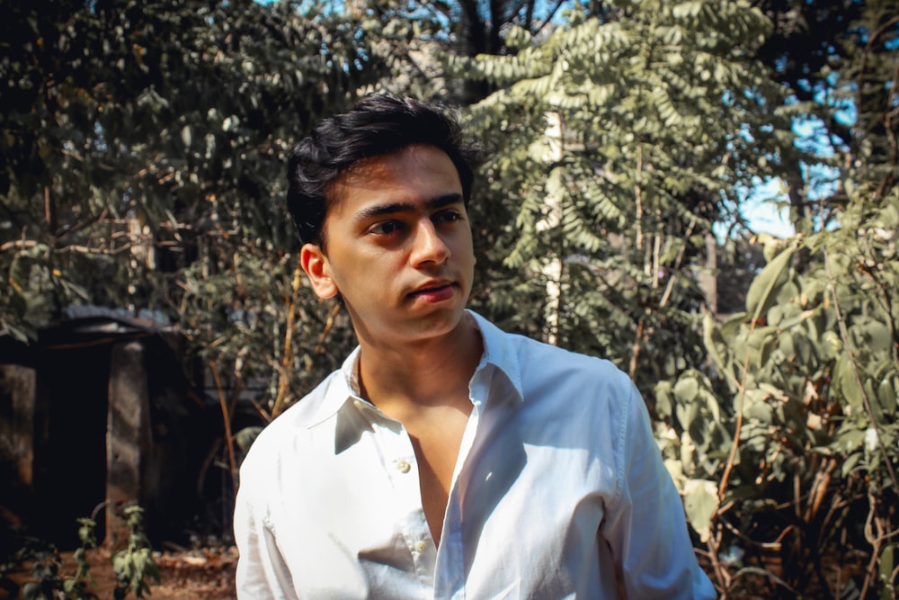 man in white dress shirt standing near green trees during daytime