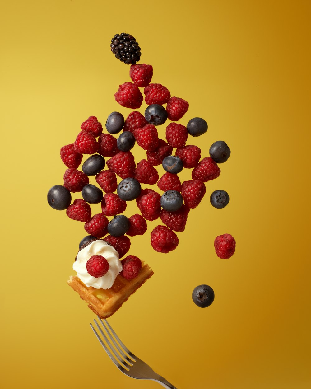 a piece of cake on a fork with berries and blueberries falling out of it