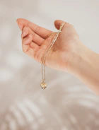 Close-up of hands holding a delicate gold pendant shaped like a heart.