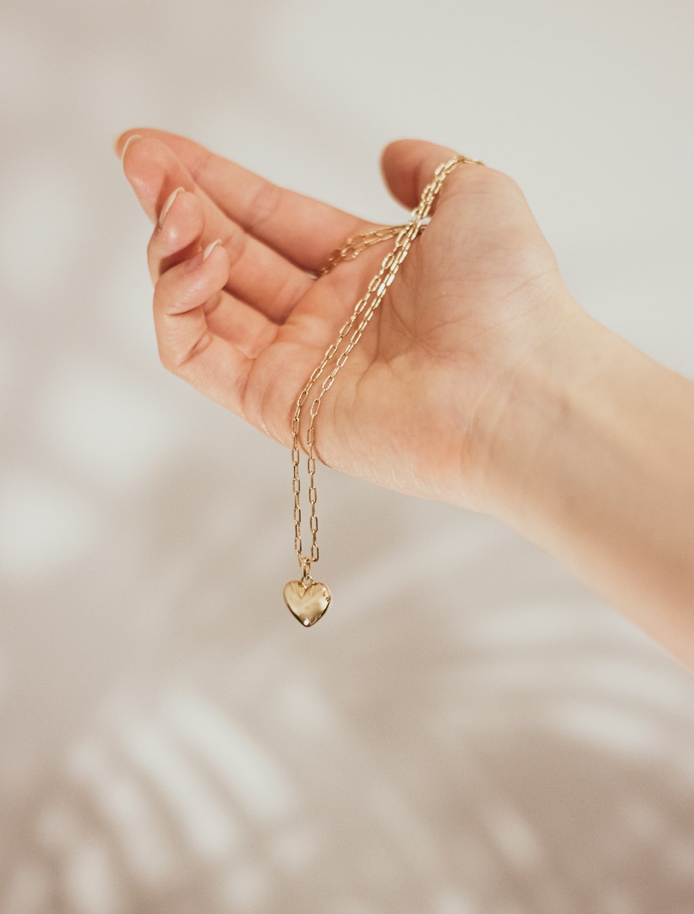 a hand holding a gold heart charm on a chain