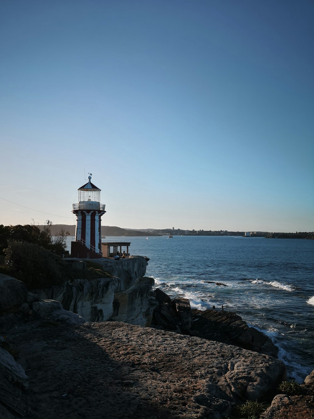 a red and white lighthouse sitting on top of a cliff next to the ocean