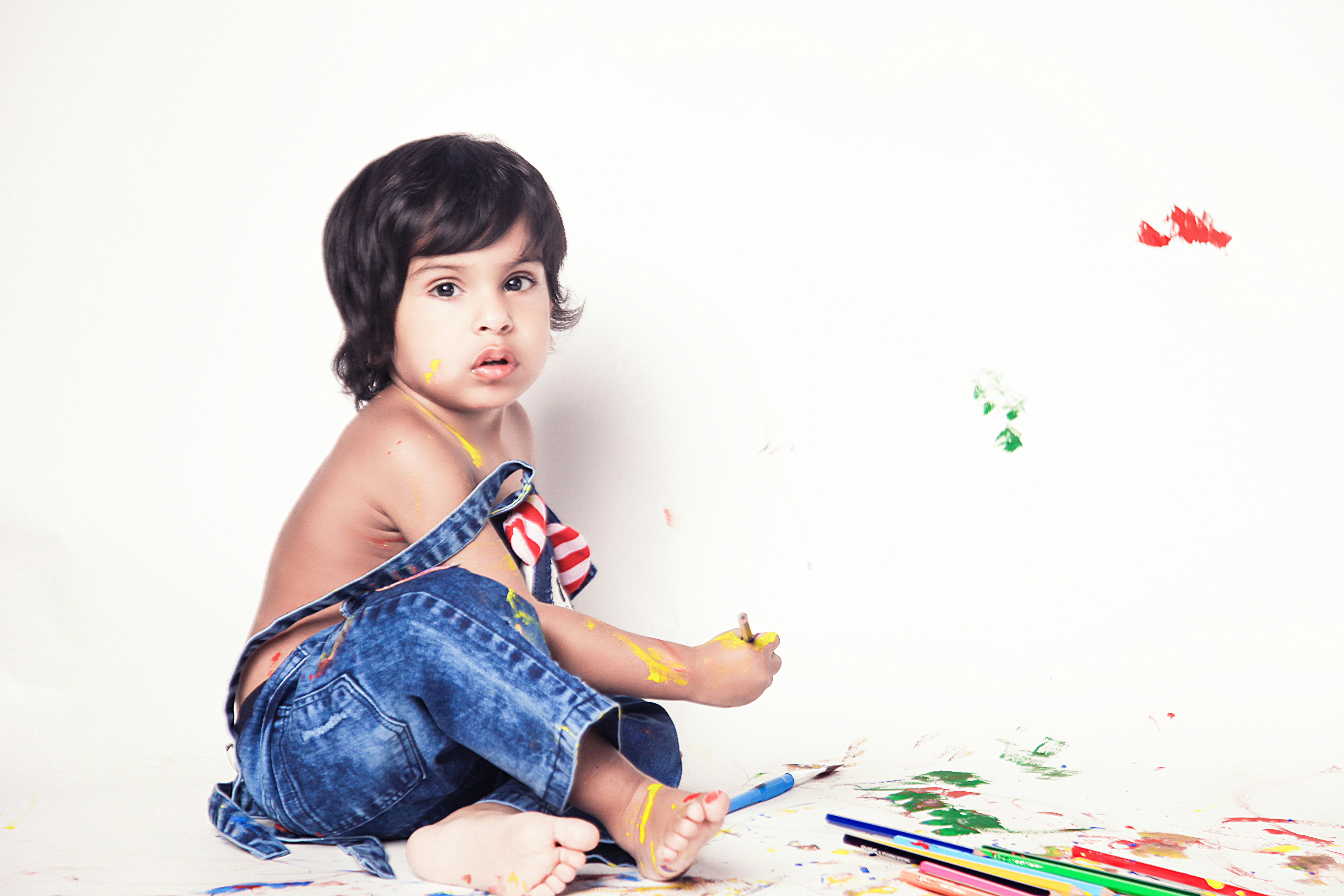 girl in blue denim dungaree sitting on white and green floral textile