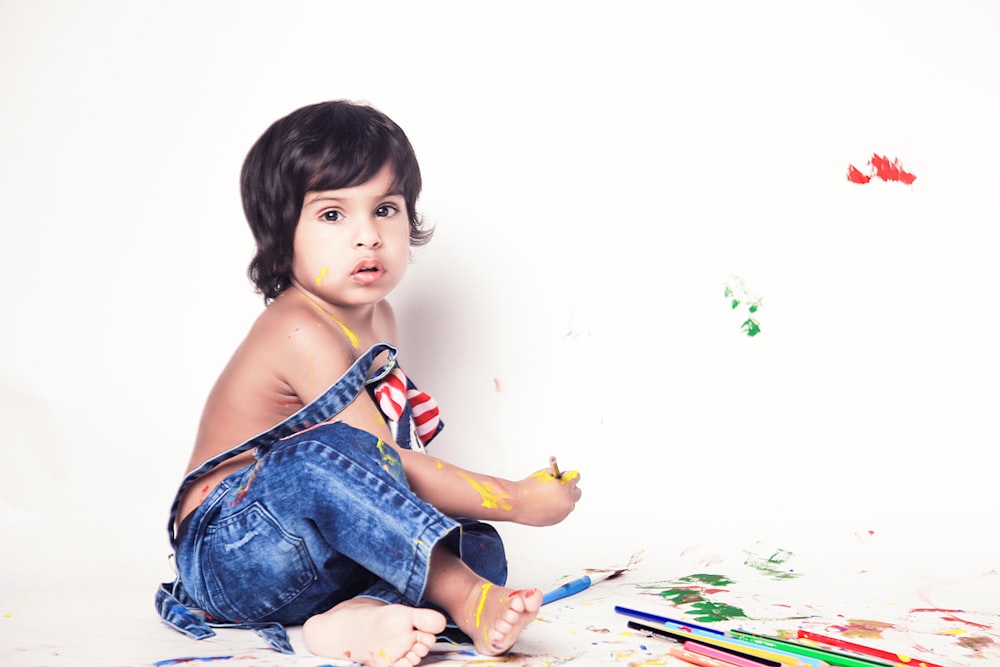 girl in blue denim dungaree sitting on white and green floral textile