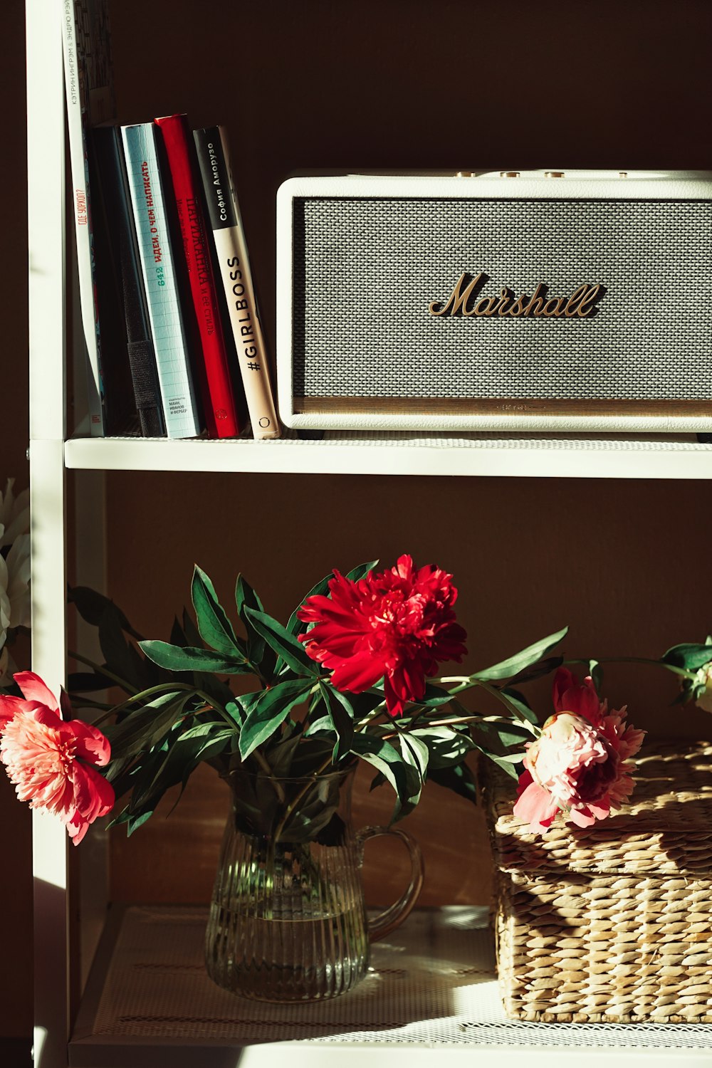 a vase filled with red flowers next to a book shelf