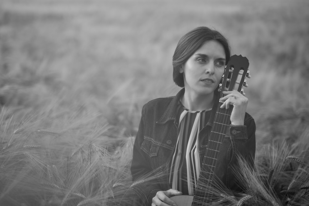 a woman sitting in a field holding a guitar
