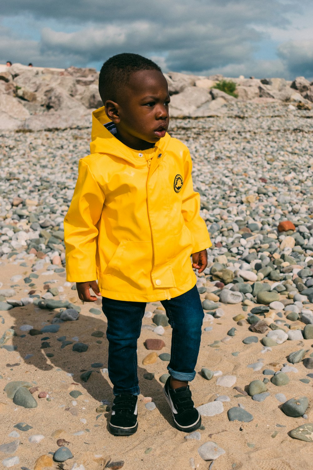 a young boy in a yellow rain coat standing on a rocky beach