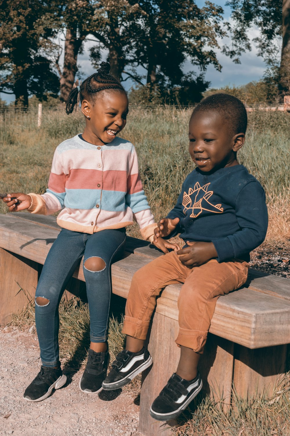 a couple of kids sitting on top of a wooden bench