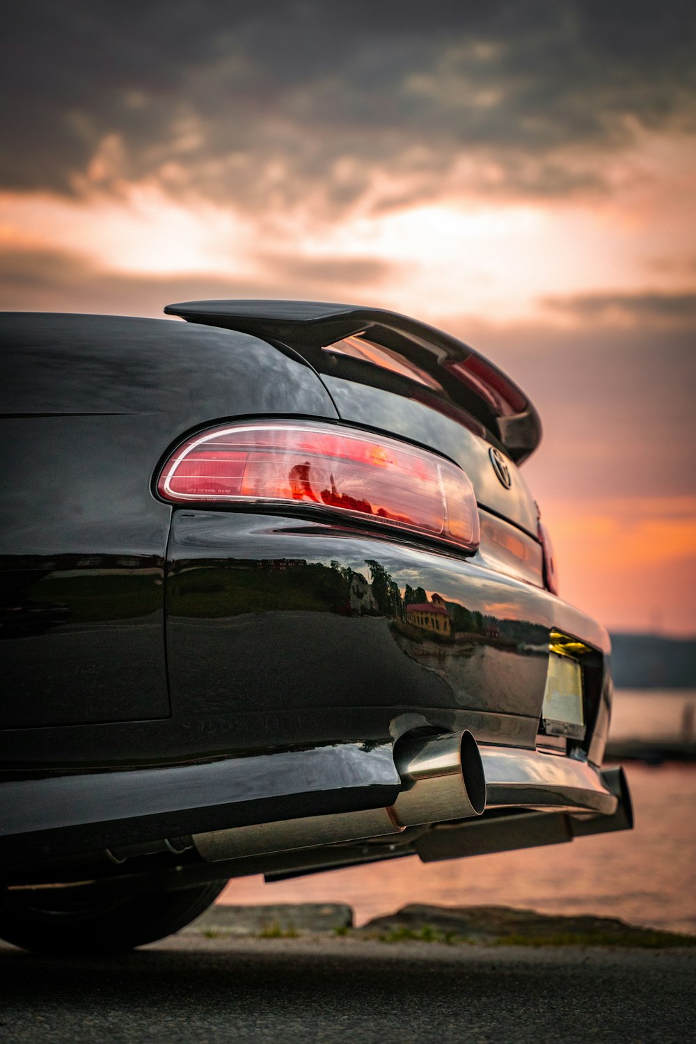 the back end of a black car with a sunset in the background