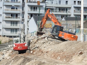 a construction site with a large orange excavator and a small red truck