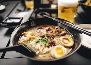 a bowl of ramen with chopsticks and a glass of beer