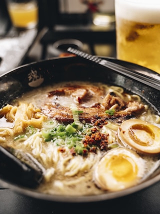 a bowl of ramen with chopsticks and a glass of beer