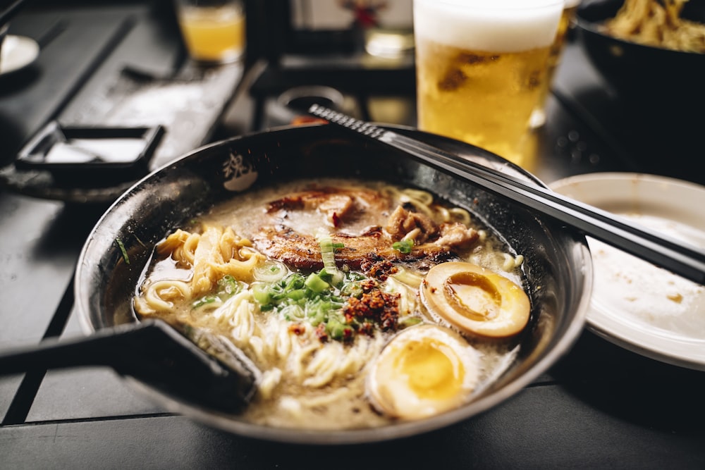 a bowl of ramen with chopsticks and a glass of beer