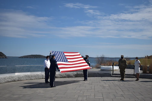 A group of veterans standing together in front of a flag-draped memorial on a clear day.
