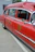 A vintage red ambulance with chrome detailing is parked outdoors next to a white container. The vehicle features the word 'AMBULANCE' and a fire department museum logo on the side. The windows are slightly tinted, and the interior appears to have old-fashioned seating.
