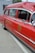 A vintage red ambulance with chrome detailing is parked outdoors next to a white container. The vehicle features the word 'AMBULANCE' and a fire department museum logo on the side. The windows are slightly tinted, and the interior appears to have old-fashioned seating.