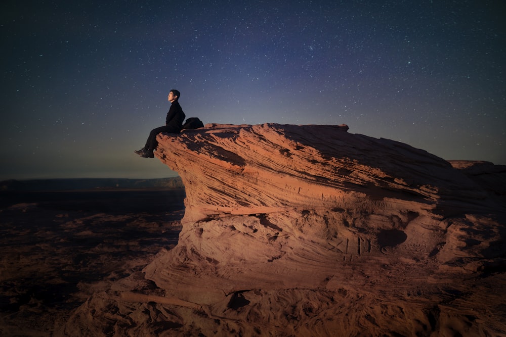 a man sitting on top of a large rock