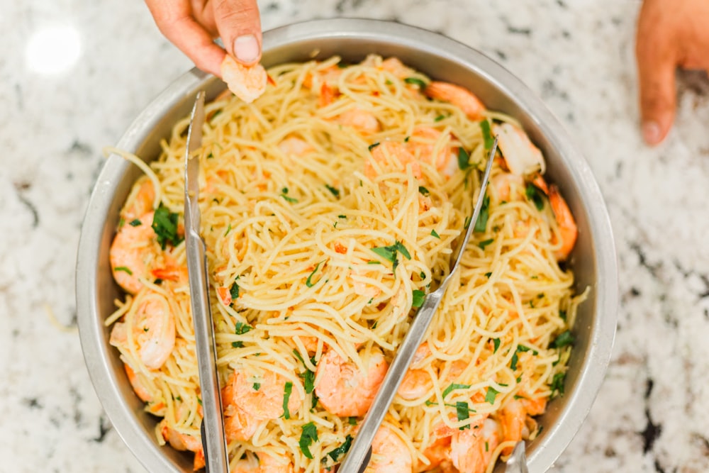 person holding stainless steel bowl with noodles