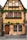 An old, charming house with a timber-frame structure and yellow-painted walls. The building features multiple windows adorned with flower boxes full of greenery, climbing ivy, and a wooden door. The street in front is cobblestoned.