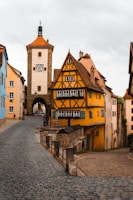 a cobblestone road with a yellow building and a clock tower in the background