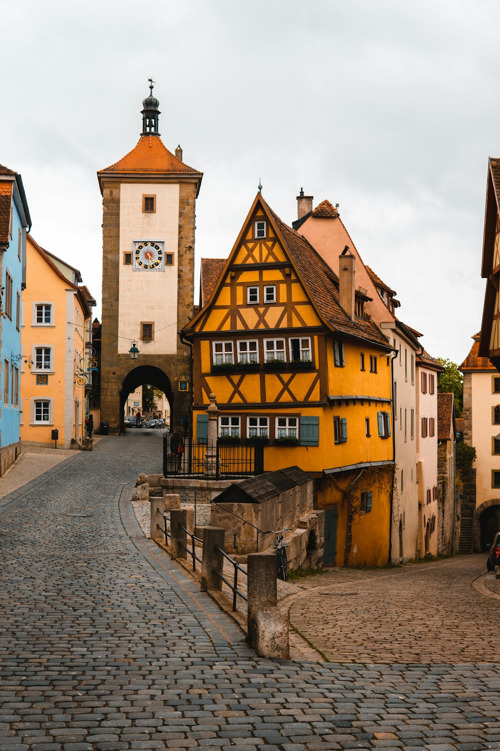 a cobblestone road with a yellow building and a clock tower in the background