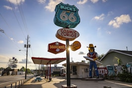 a statue of a cowboy holding a surfboard in front of a gas station