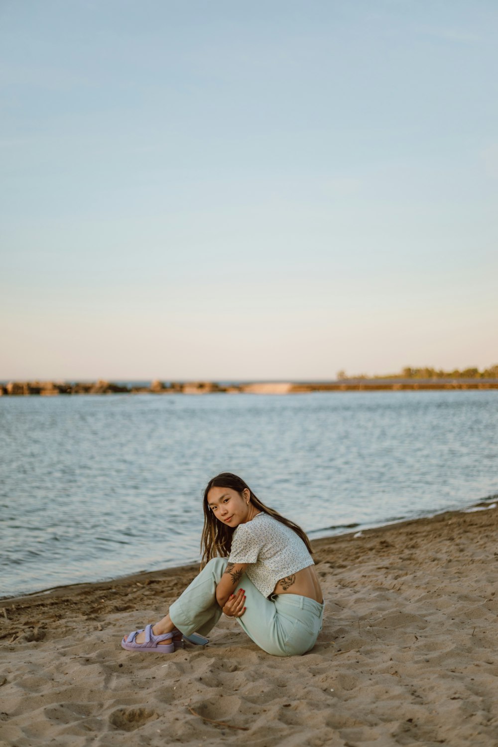 a woman sitting on a beach next to a body of water