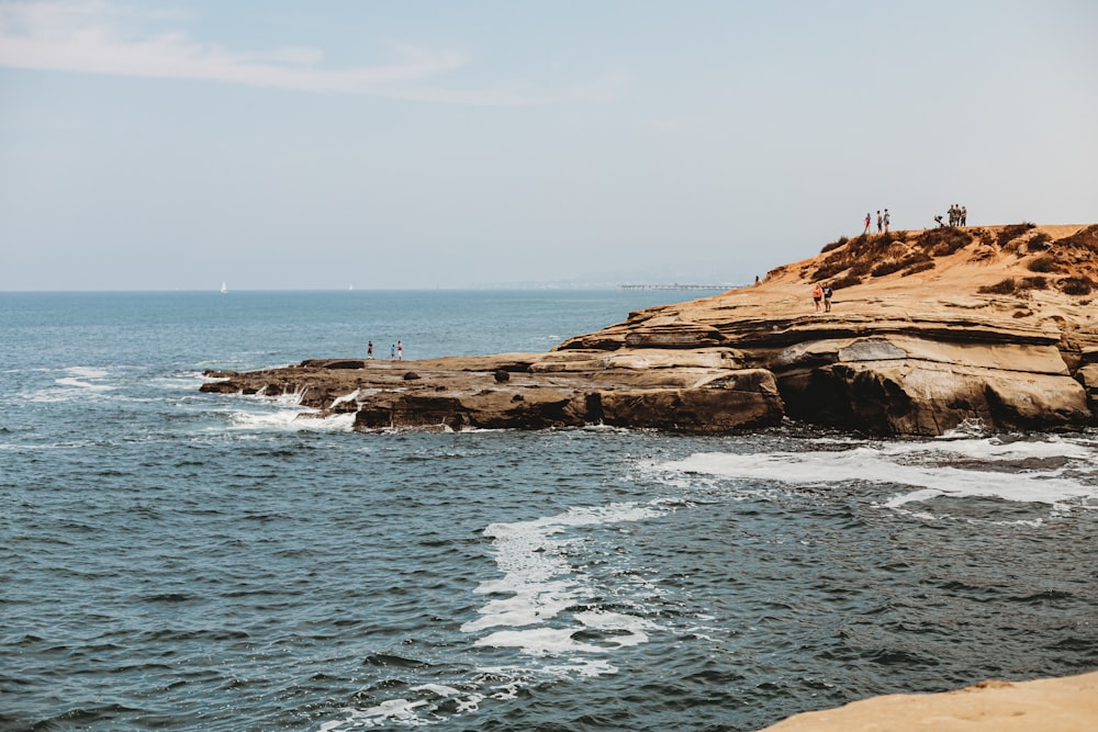 people standing on brown rock formation near body of water during daytime