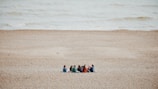 a group of people sitting on top of a sandy beach