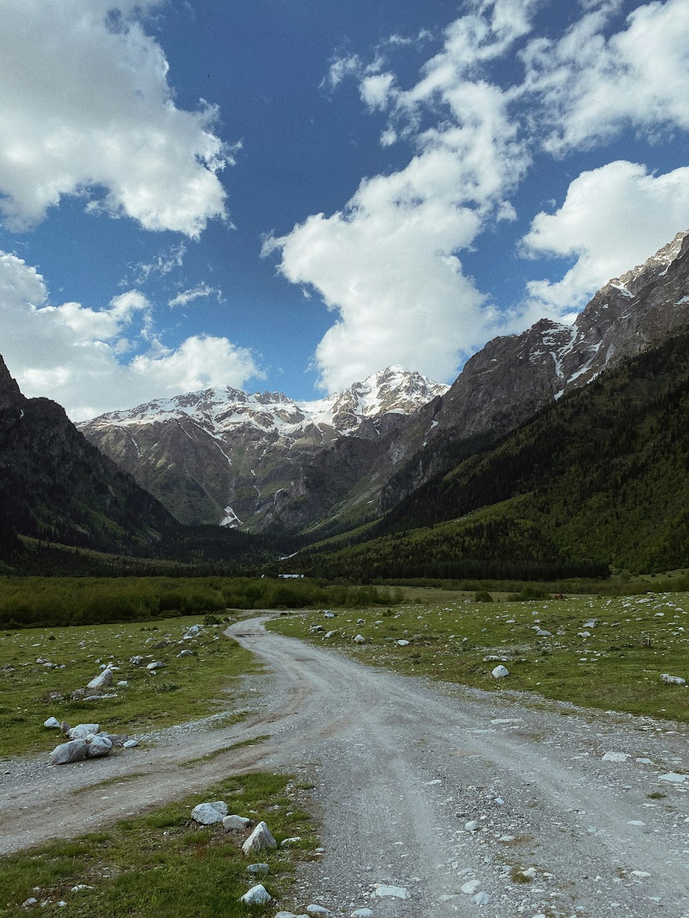 green grass field and mountains under blue sky and white clouds during daytime