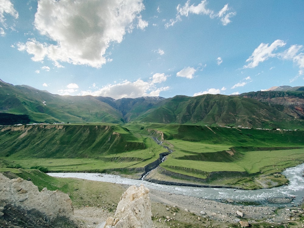 green grass field and mountains under white clouds and blue sky during daytime