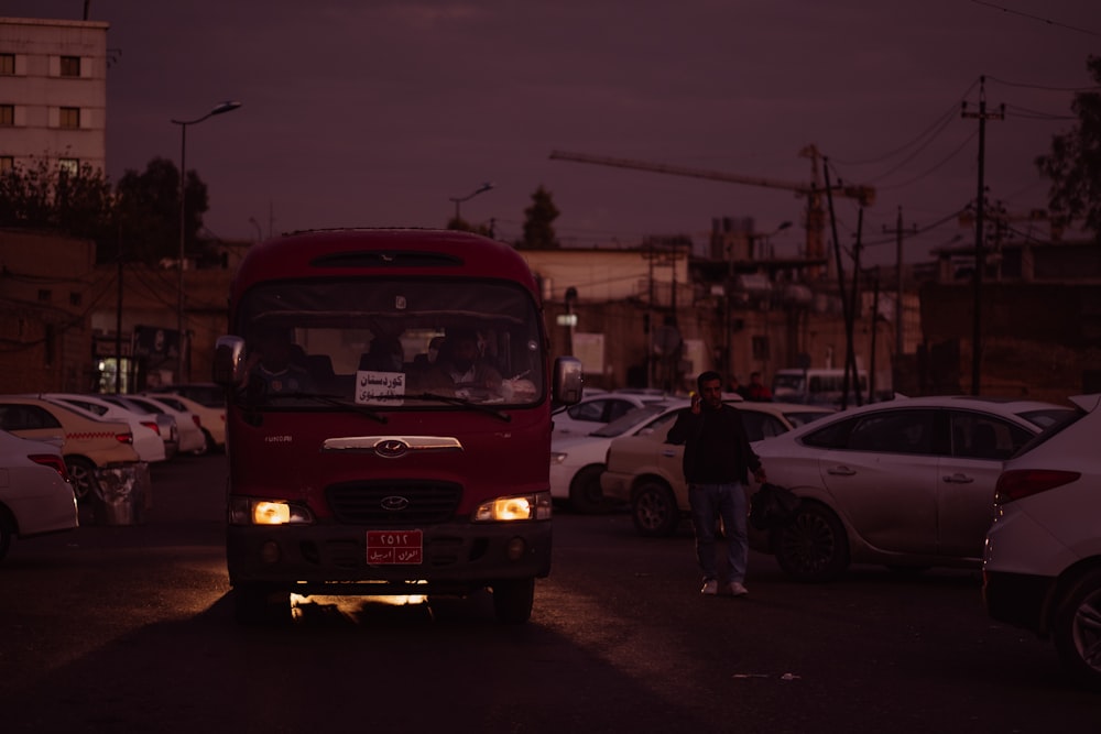 a red bus driving down a street next to parked cars