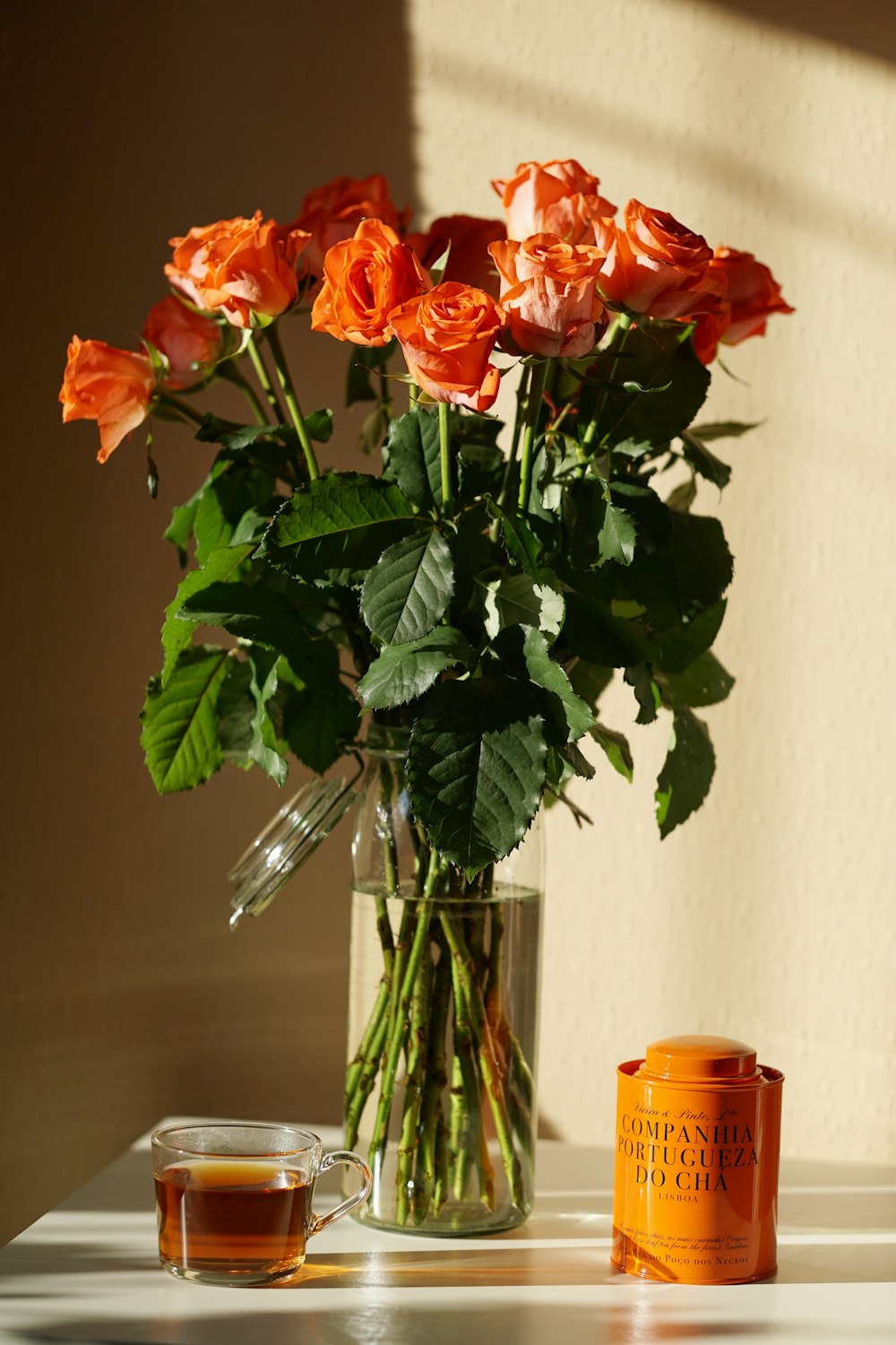 a vase filled with orange roses next to a cup of tea